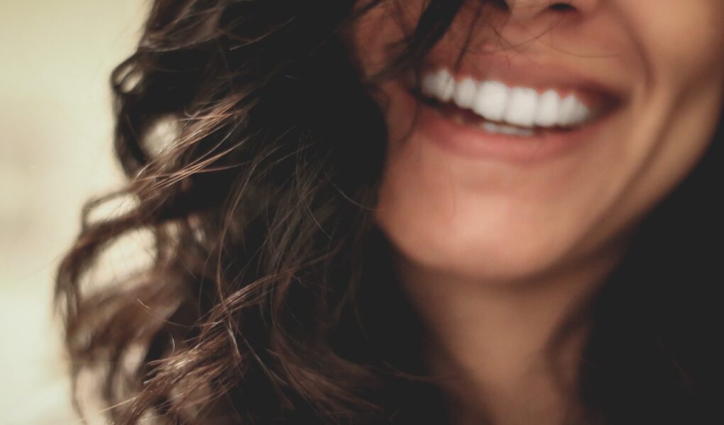 A woman with long wavy black hair smiling with visible white teeth